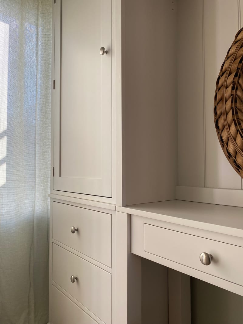 Detail of the join between the left cupboard and the dressing table, showing the panelled door, brushed nickel knobs, drawer fronts and the desk edge beside the mirror