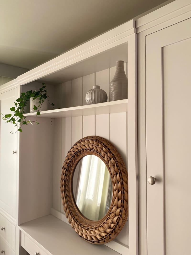 View of the upper section showing the display shelf with two ribbed grey vases and a trailing ivy, the round rattan mirror on the boarded back below and the cupboard door knob to the right