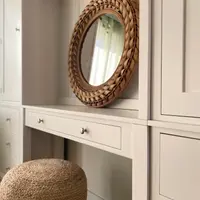 Angled close view along the dressing table top, showing the rattan mirror sitting against the boarded back, the single wide drawer with two knobs and the jute pouffe beneath