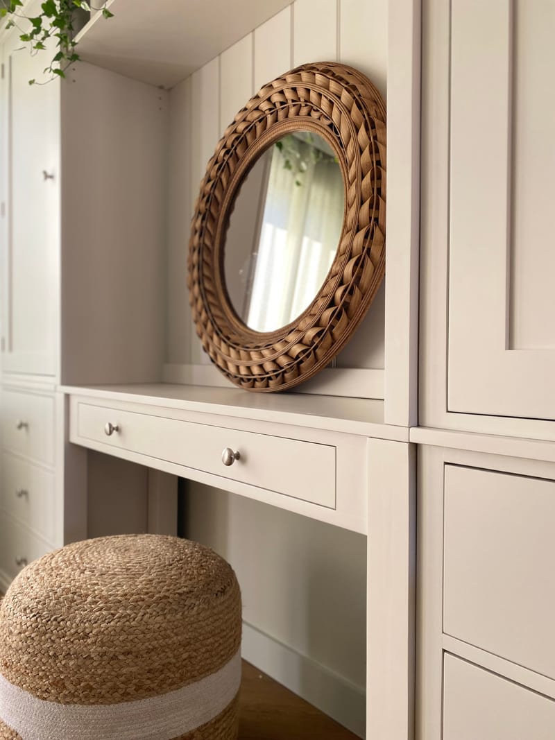 Angled close view along the dressing table top, showing the rattan mirror sitting against the boarded back, the single wide drawer with two knobs and the jute pouffe beneath