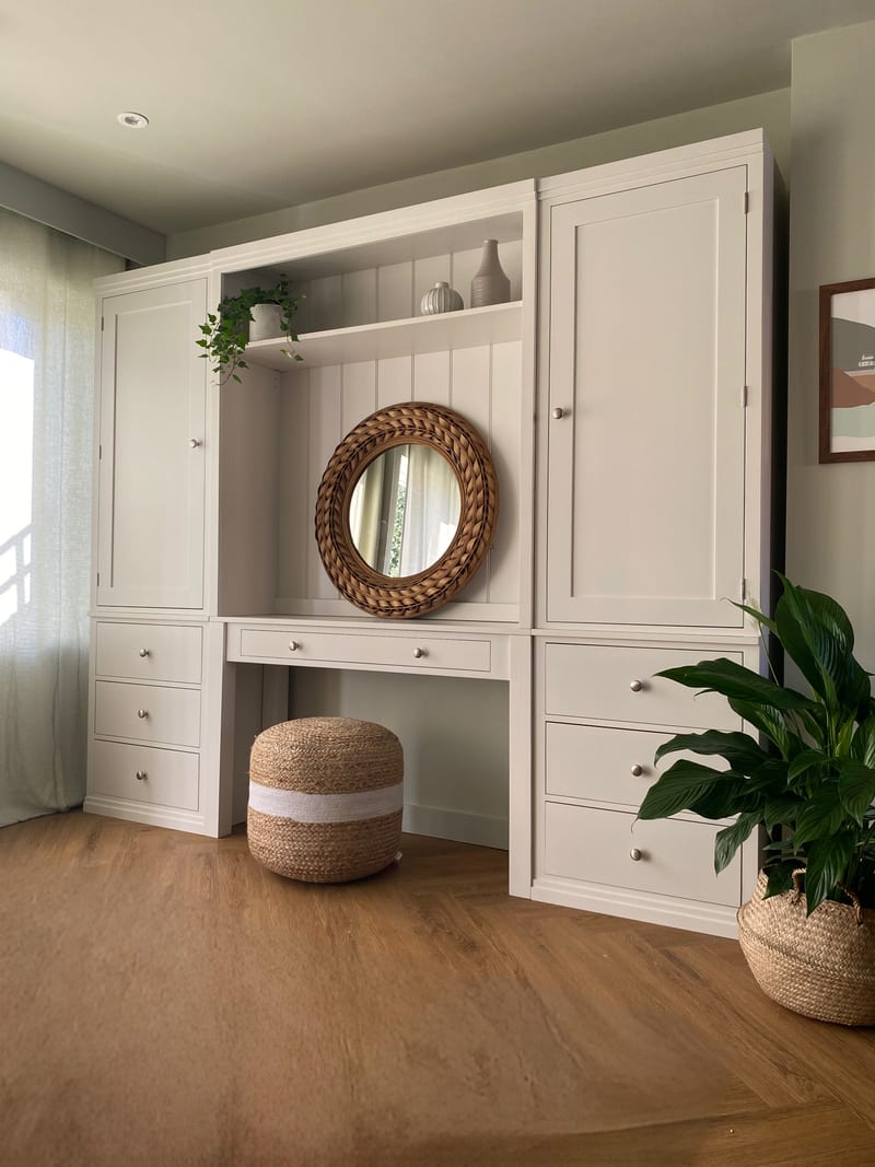 Front view of the complete unit with the wood-effect floor sweeping across the foreground, the jute pouffe under the desk and a peace lily in a woven basket to the right