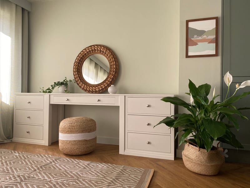 Straight-on view of the soft greige painted dressing table with two three-drawer pedestals and a wide centre drawer, brushed nickel knobs, a round rattan mirror above and a jute pouffe beneath