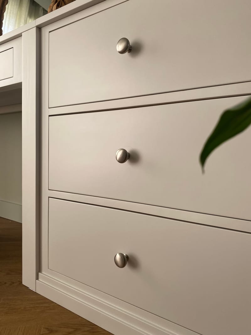Close view of the right-hand pedestal, showing three deep drawers with brushed nickel knobs, the moulded plinth, the slim desk drawer alongside and a peace lily leaf in front
