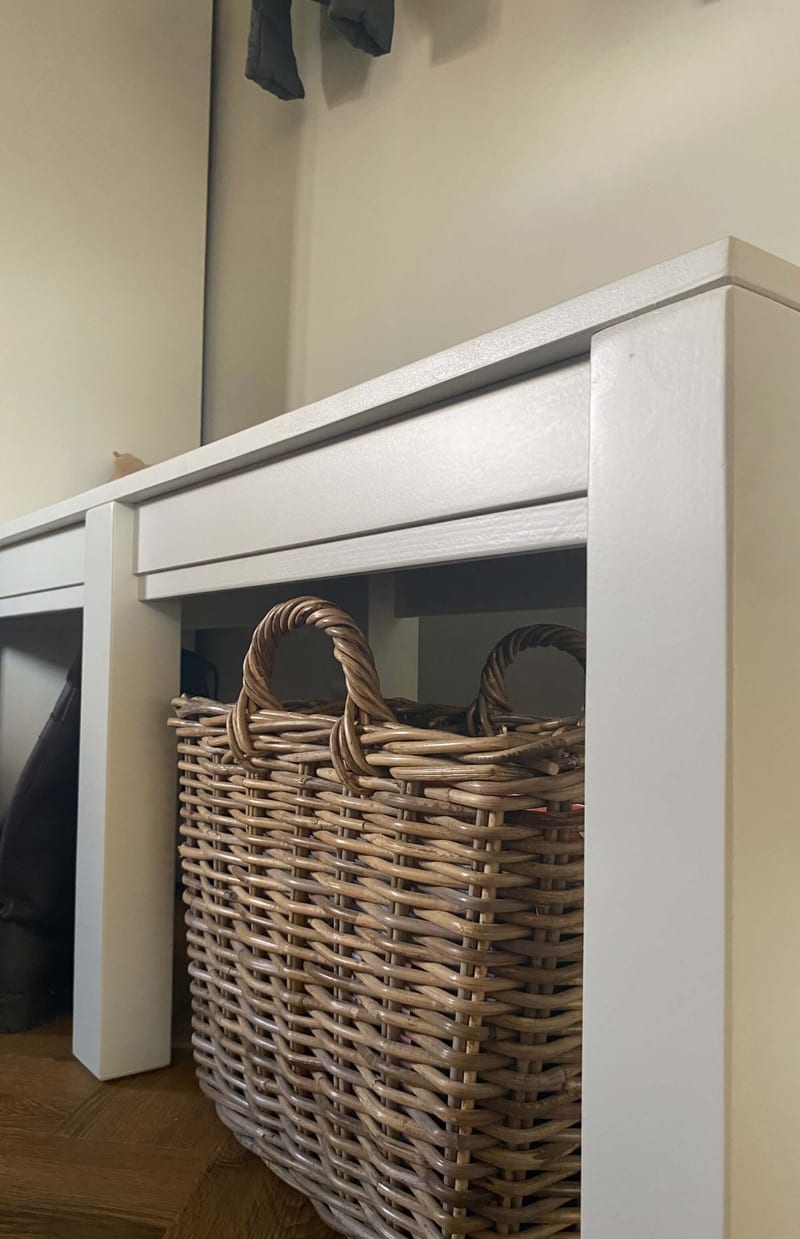 Corner detail of the two benches at seat level, showing the square leg, the overhanging seat top and the apron rail, with a large kubu wicker basket stored in the space underneath
