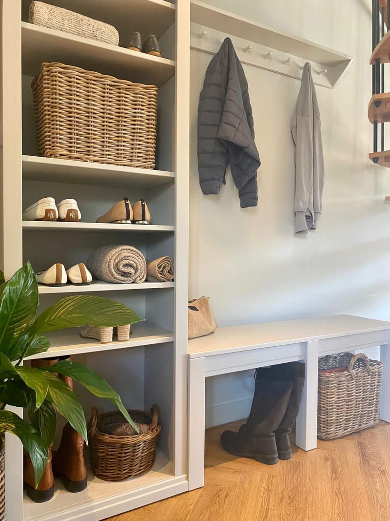 Close view of the middle shelves holding a kubu basket, white loafers, tan mules and rolled throws, with the peg rail, two coats and the bench with boots and a basket beyond