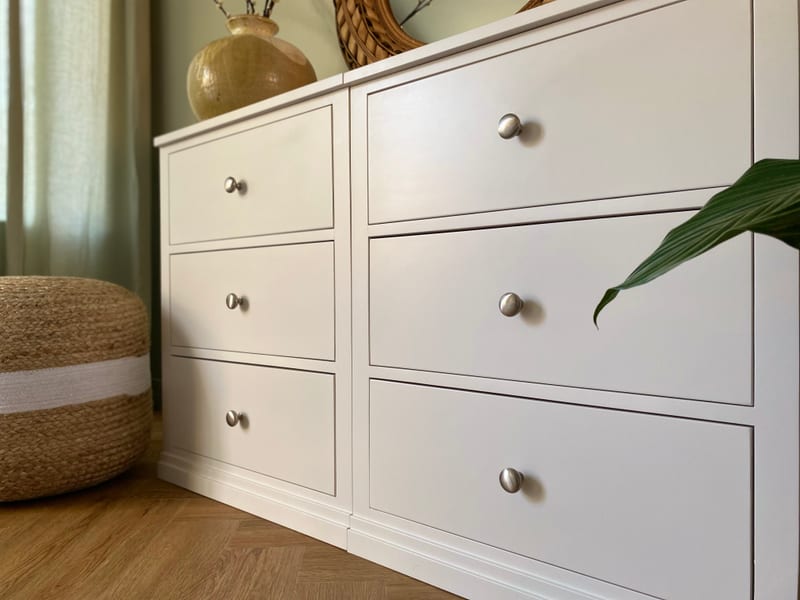 Close angled view across the drawer fronts, showing the two joined modules, the fine shadow gaps between the drawers, brushed nickel knobs and the moulded plinth at floor level