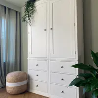 White painted Colmworth modular double wardrobe with two tall panelled doors above six drawers, with trailing ivy on top and a jute pouffe alongside