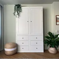 Full front view of the white painted double wardrobe against a pale green wall, showing two tall panelled doors, six drawers with round brushed nickel knobs and a diamond patterned rug in front