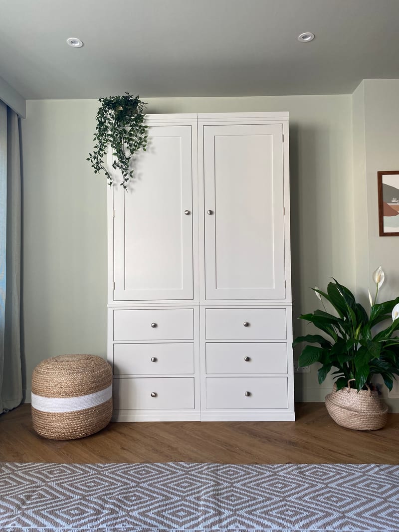 Full front view of the white painted double wardrobe against a pale green wall, showing two tall panelled doors, six drawers with round brushed nickel knobs and a diamond patterned rug in front