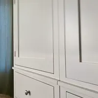 Close view along the front of the white painted wardrobe doors, showing the recessed panel mouldings, the narrow door gaps, a brushed nickel drawer knob and the moulded shelf above the drawers