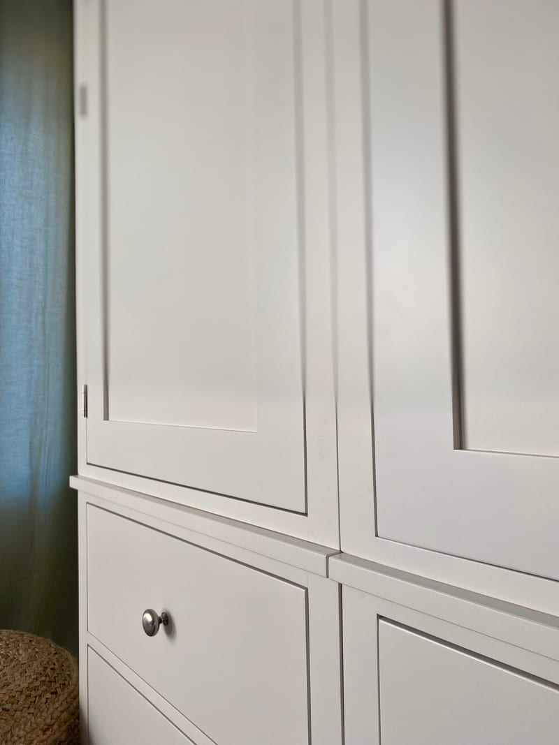Close view along the front of the white painted wardrobe doors, showing the recessed panel mouldings, the narrow door gaps, a brushed nickel drawer knob and the moulded shelf above the drawers