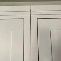 Detail of the tops of the two white painted wardrobe doors, showing the stepped cornice beading, the panel mouldings and the narrow gap where the doors meet below the shadowed ceiling