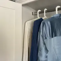 Close view inside the open wardrobe, showing the chrome hanging rail on its bracket, white hangers and a cream blouse, a navy knit and a blue satin shirt hanging below the moulded cornice