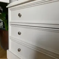 Angled close view of the three drawer fronts of the cream painted wardrobe, showing the moulded edges, round brushed nickel knobs and the moulded plinth above oak flooring