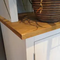 Close-up of the corner of the pine worktop, showing the grain and squared edge beside a ribbed terracotta plant pot, with the white painted side and a steel door hinge below