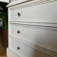Close angled view of the three drawers on the larder base, showing the beaded panel mouldings, brushed nickel knobs and the stepped plinth above the oak floor