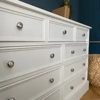Low angled view along the off-white drawer fronts, showing the moulded panel edges and rows of brushed nickel knobs receding towards the deep navy wall and woven basket