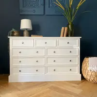 Full front view of the off-white nine-drawer chest, three short drawers above three rows of paired wide drawers, all with brushed nickel knobs, on light oak herringbone parquet