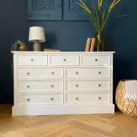 Full front view of the off-white nine-drawer chest of drawers, three short drawers above three rows of paired wide drawers with brushed nickel knobs, on oak herringbone parquet