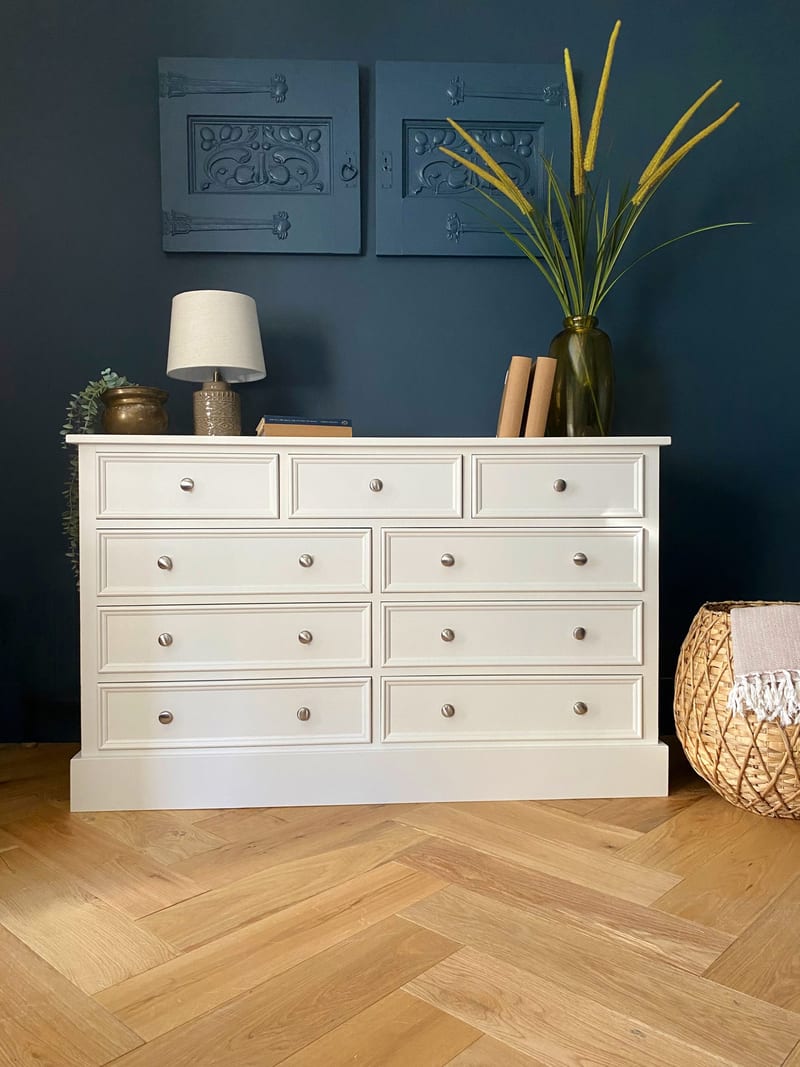 Full front view of the off-white nine-drawer chest of drawers, three short drawers above three rows of paired wide drawers with brushed nickel knobs, on oak herringbone parquet