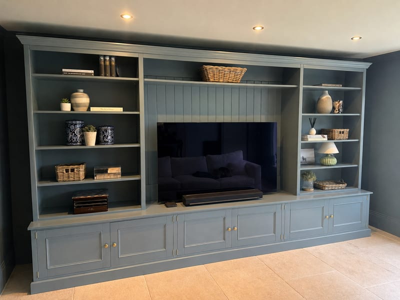 Full angled view from the left, showing the moulded cornice, the tall open bookcases either side of the recessed television and the long run of panelled cupboards on the stone floor tiles