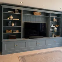 View past a black steel-framed internal door with the staircase visible through its glass, looking across the tiled floor to the shelving, television recess and brass-knobbed cupboards