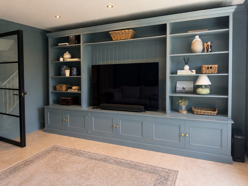 Angled view from the right along the length of the piece, the open shelves styled with pottery, books and baskets, and the soundbar on the worktop below the television