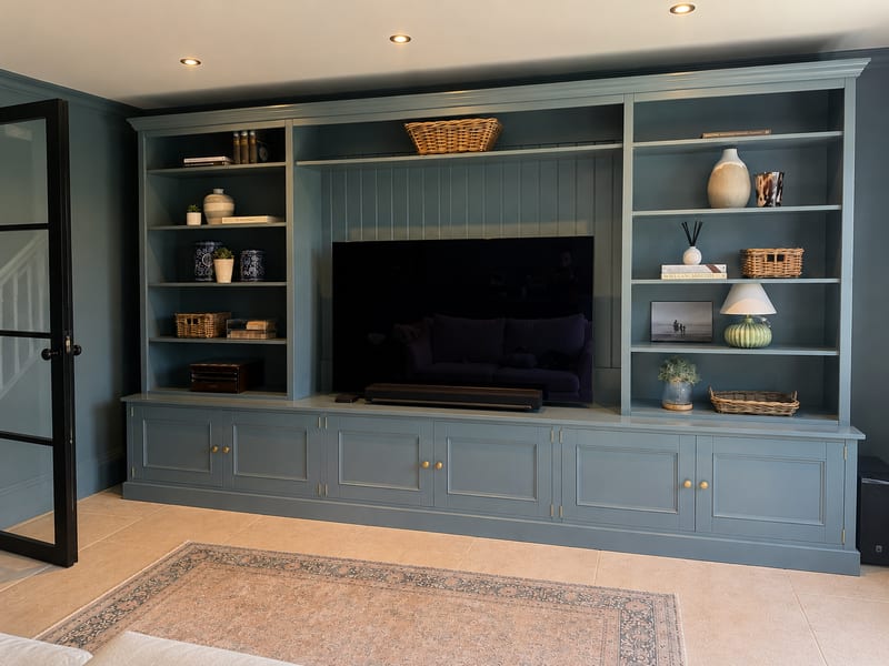 Wider view from the right with the dark blue-grey walls and ceiling spotlights, the patterned rug in the foreground and a black subwoofer standing beside the right-hand bookcase