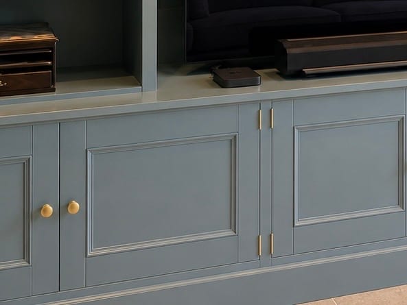 Close view of the panelled cupboard doors below the worktop, showing the brass knobs, brass butt hinges and beaded panel mouldings, with a set-top box and soundbar on the surface above