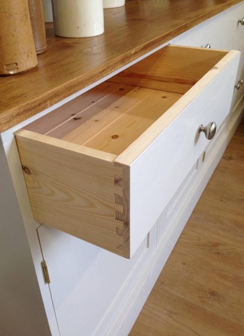Detail of a drawer pulled out of the white painted base, showing the hand-cut dovetail joints, solid pine drawer box and brushed nickel knob beneath the waxed pine top