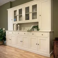 Angled view of the cream painted dresser against an olive green wall, showing four glazed doors between two tall solid end doors, with three drawers and six panelled cupboards below