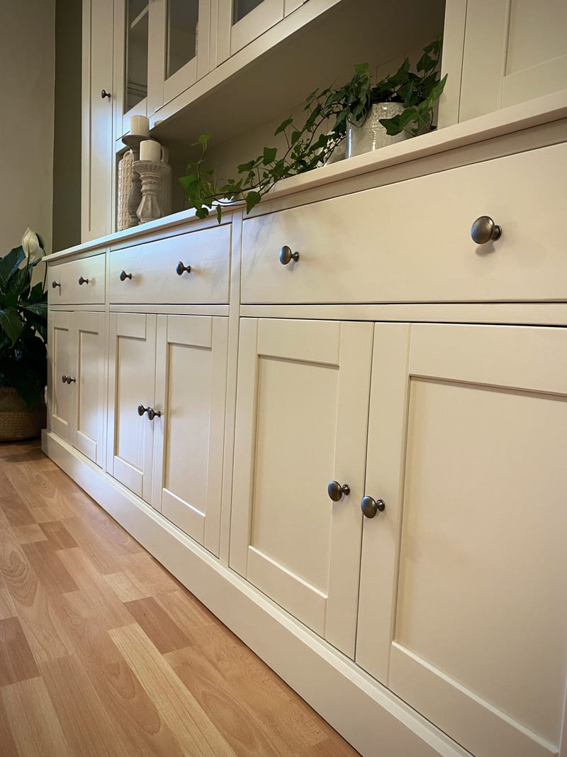 Low angled view along the base, showing the drawer fronts and shaker panelled doors with dark aged bronze knobs, a peace lily to the left and candlesticks on the worktop above