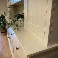 Close view across the painted cream worktop to the solid right-hand door, showing the shaker panel, trailing ivy and the aged bronze knobs on the drawers beneath