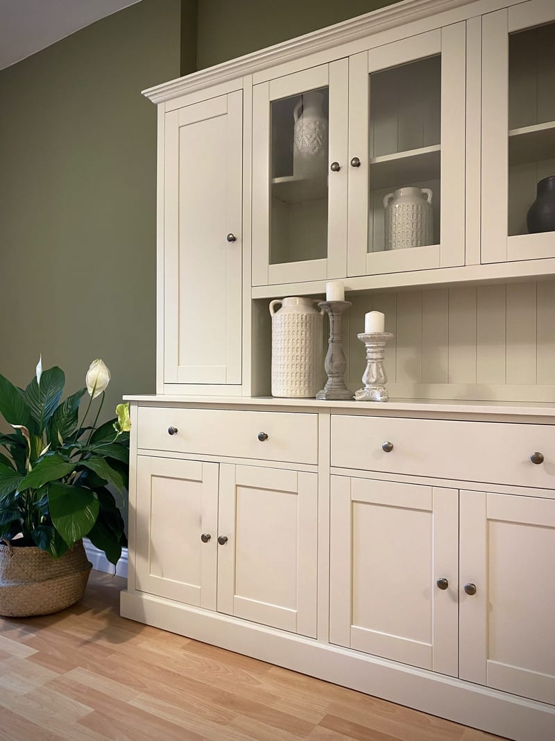 View of the left-hand end, showing the solid upper door beside the glazed cupboards, candlesticks and a jug on the shelf, and the drawers and panelled doors below