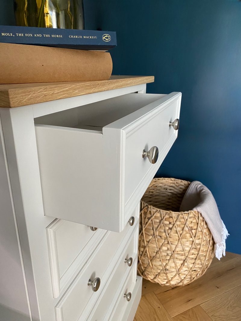 Top drawer pulled open to show the depth of the drawer box, with a stack of books on the oak top and a woven basket of throws on the herringbone oak floor