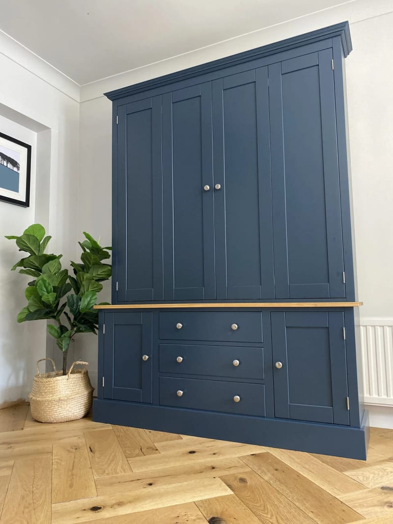 Navy blue painted TV dresser with bifolding doors closed across the top section, a solid oak worktop, and three drawers between two cupboards in the base, on herringbone oak flooring