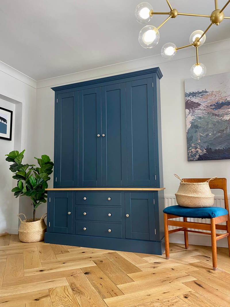 Navy blue painted TV dresser with bifolding doors closed across the top section, a solid oak worktop, and three drawers between two cupboards in the base, on herringbone oak flooring