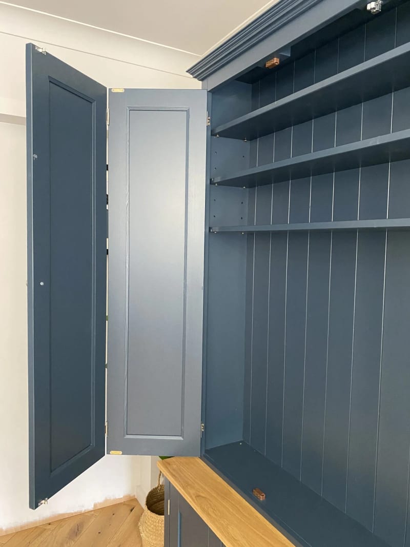 Close view of one pair of bifolding doors folded flat against the side, showing the brass butt hinges and the shelved tongue-and-groove interior above the oak worktop