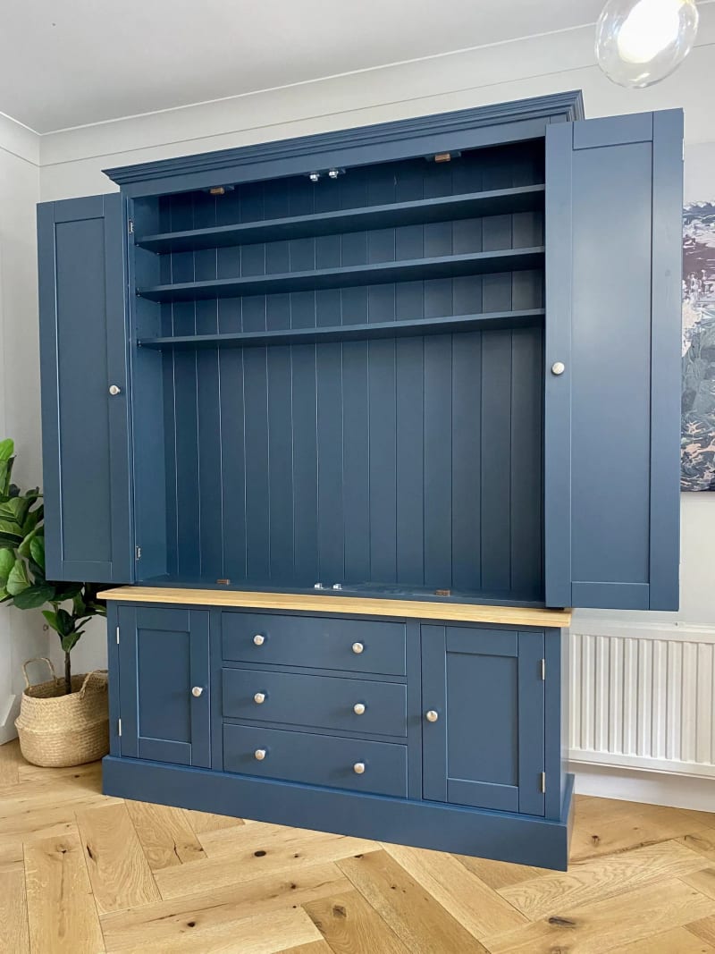 Angled view of the unit with all four doors open, showing the empty shelved top section and the base of three drawers between two cupboards on herringbone oak flooring