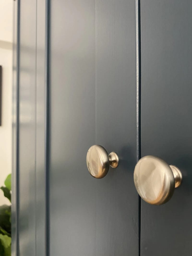Macro view of the two round brushed nickel knobs on the central pair of doors, showing the shallow gap between them and the flat panelled navy painted fronts