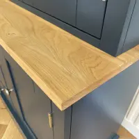 Close view of the corner of the solid oak worktop, showing its thickness and open grain where it meets the navy upper section and a cupboard door with a nickel hinge