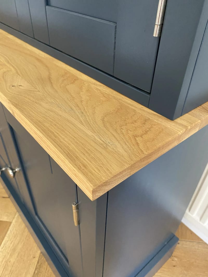 Close view of the corner of the solid oak worktop, showing its thickness and open grain where it meets the navy upper section and a cupboard door with a nickel hinge