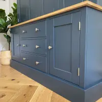 Low angled view of the base, showing three drawers flanked by two shaker cupboard doors, the oak worktop and deep plinth, with a potted plant on the herringbone floor