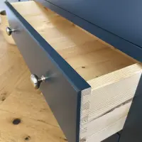Drawer pulled fully open, showing the natural pine drawer box and hand-cut dovetail joints behind the navy painted front with its round brushed nickel knob, above a herringbone oak floor