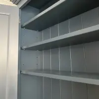 Close view inside the top section, showing three painted shelves on adjustable pegs, the tongue-and-groove back boards and a small copper coloured cable clip at the top