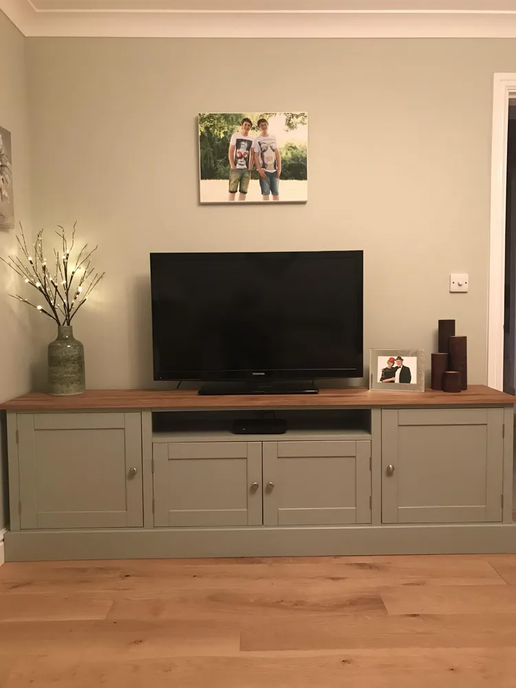 Sage green television unit with an oak top and cupboards either side of an open shelf
