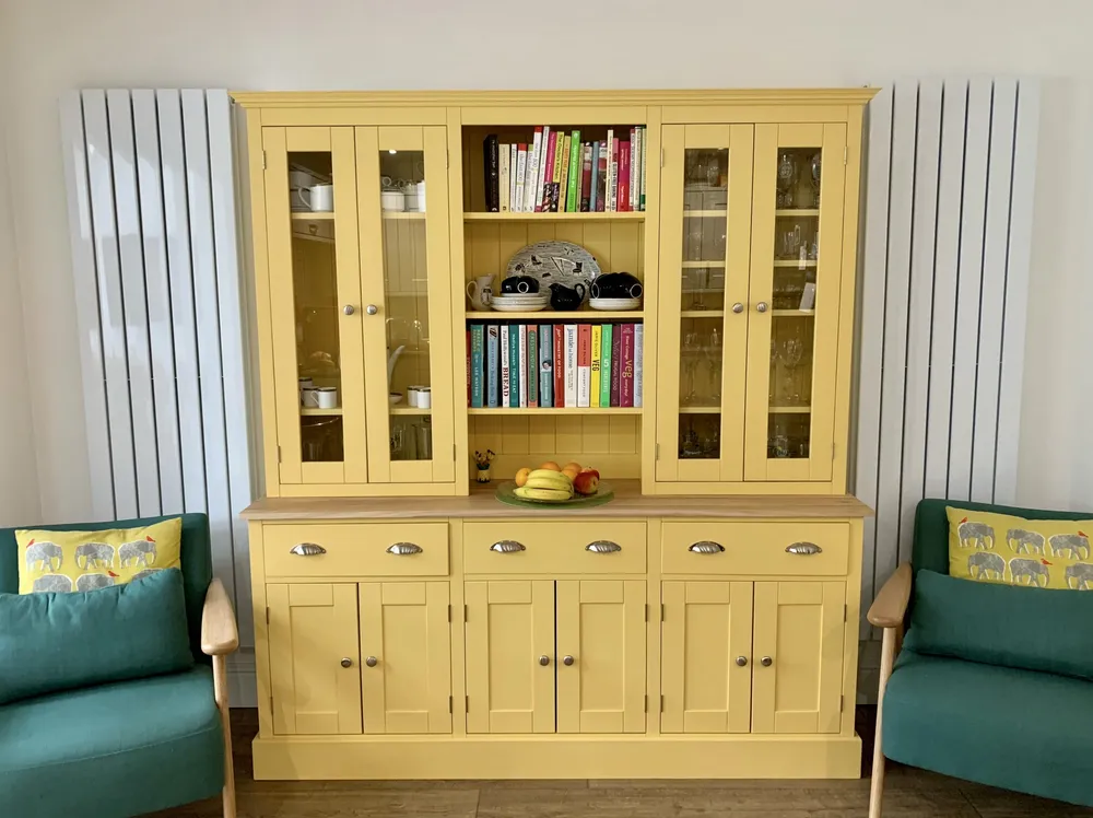 Yellow painted welsh dresser with glazed doors and an oak top in a kitchen diner