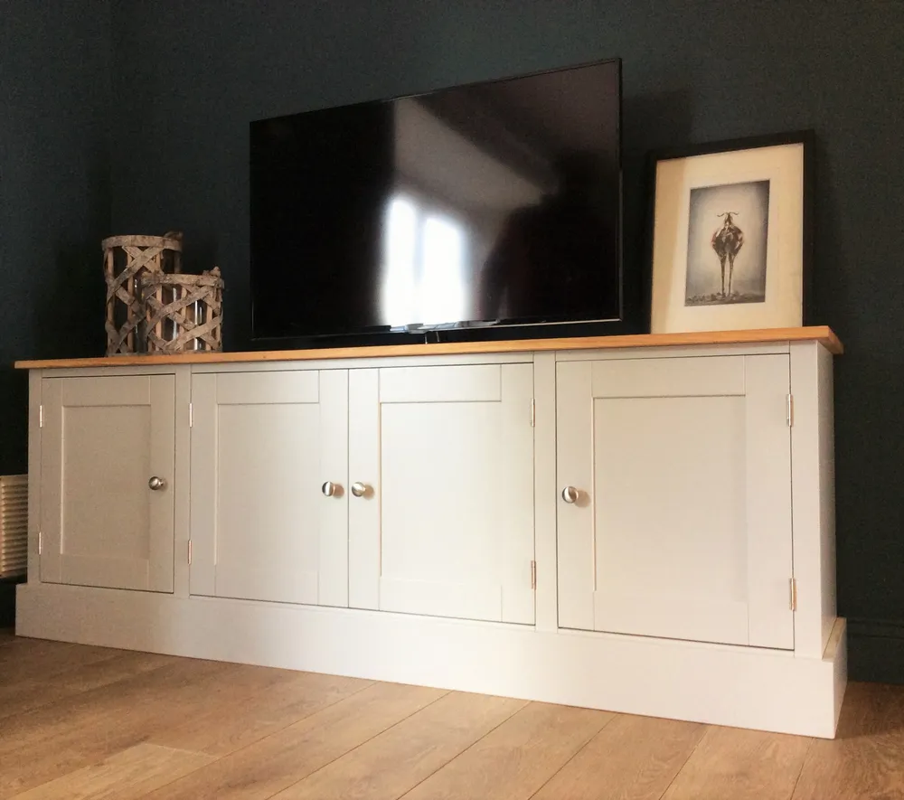 Cream painted TV cabinet with four shaker doors and an oak top against a dark wall